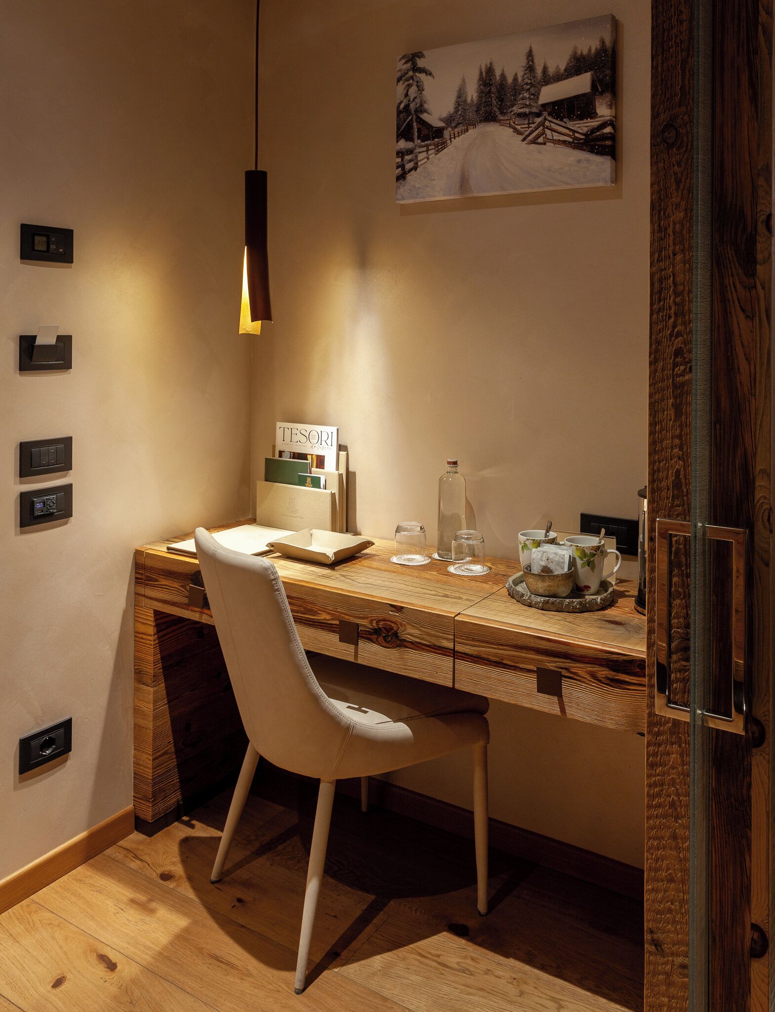 Un espacio de trabajo acogedor con un escritorio de madera, una silla blanca, una lámpara colgante y un cuadro en la pared.