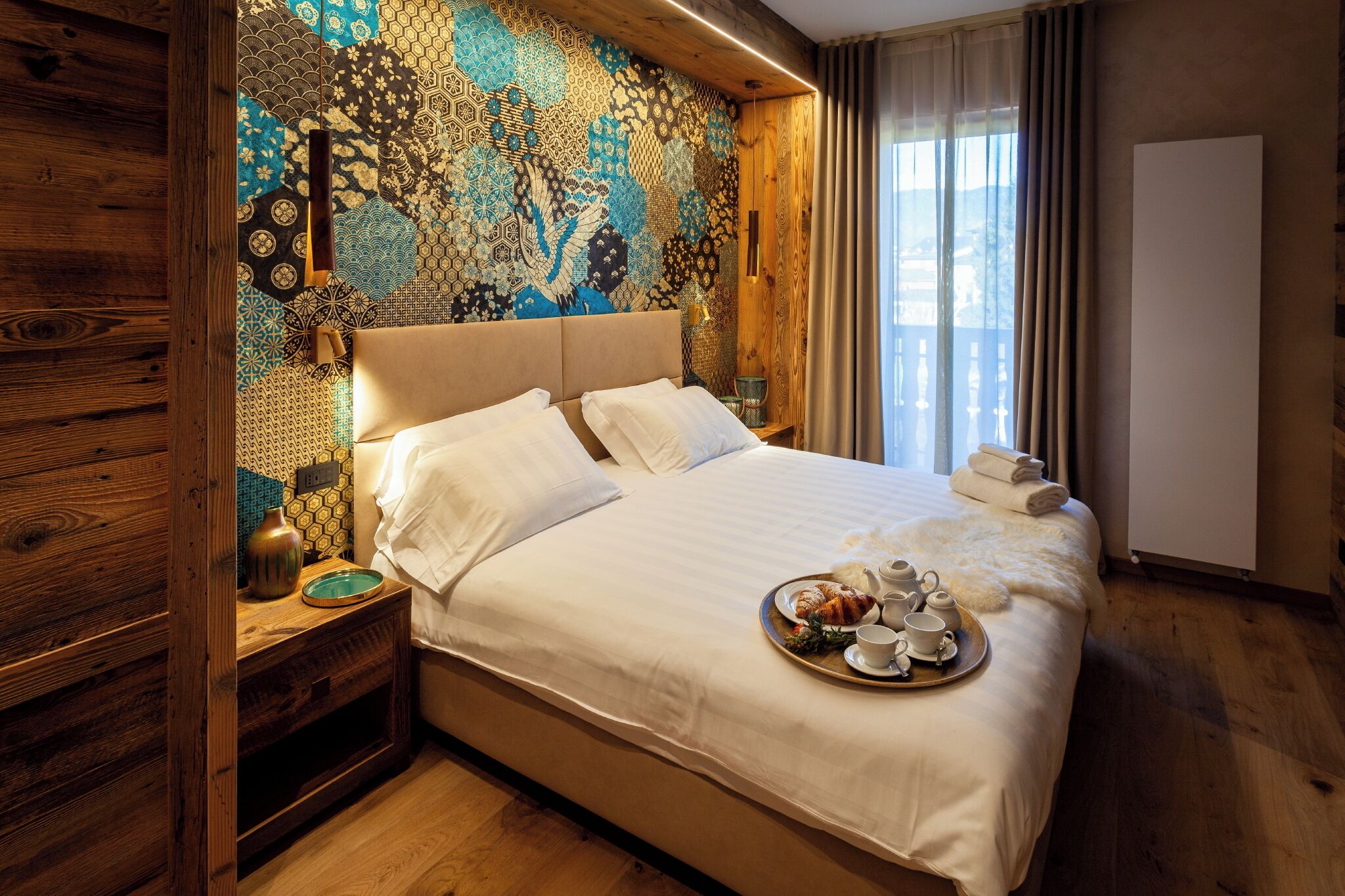 A hotel room with a large bed, a wooden headboard, a patterned wall, and a tray of breakfast items.