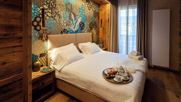 A hotel room with a large bed, a wooden headboard, a patterned wall, and a tray of breakfast items.