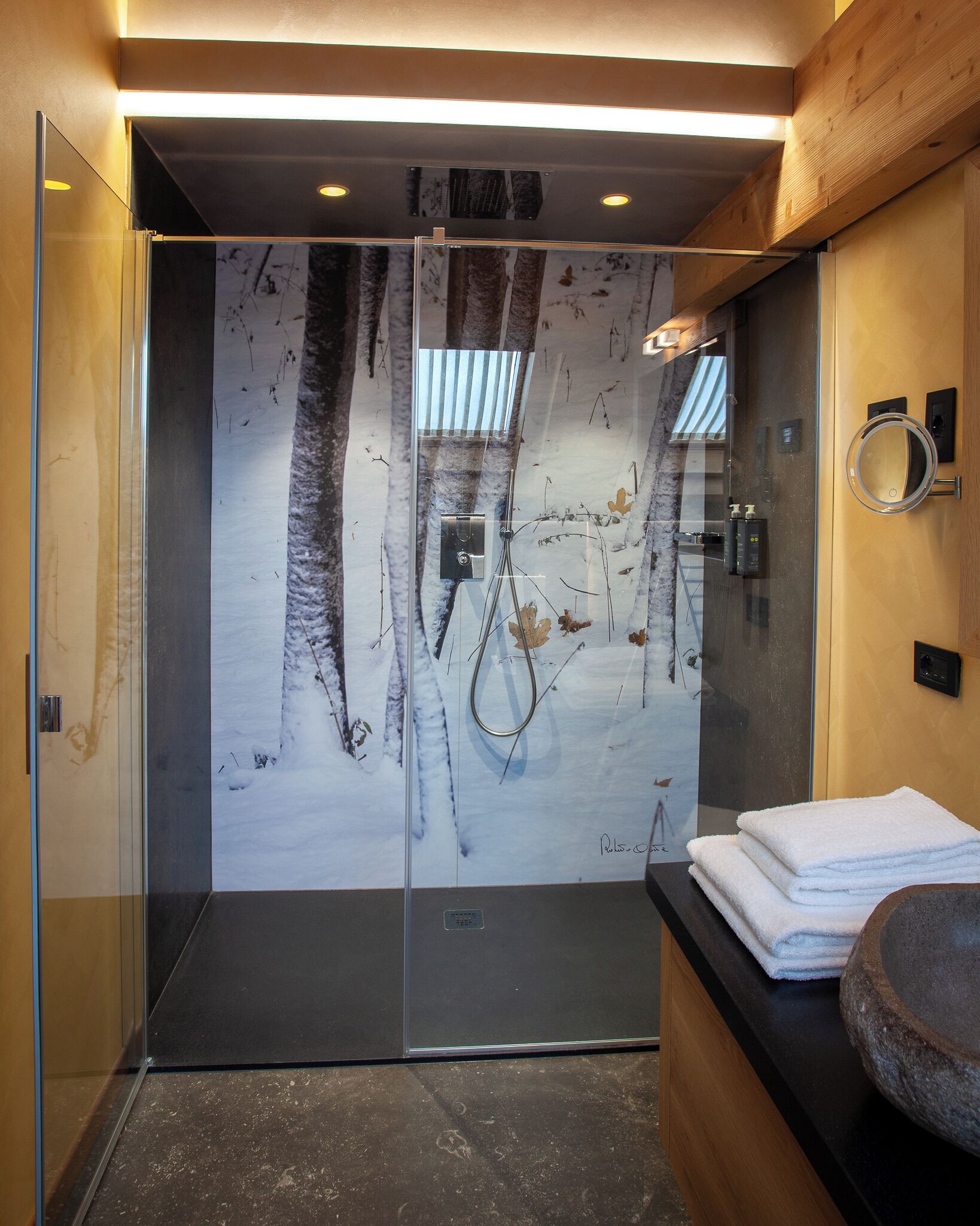 Un baño moderno con cabina de ducha de vidrio, tocador de madera y salpicadero de mármol.