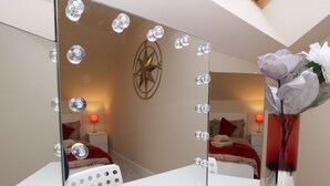 A room with a vanity mirror, a red lamp, and a vase with a flower.