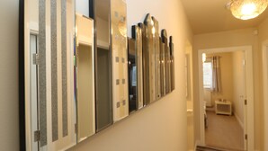 A hallway with a series of mirrors on the wall, a carpeted staircase, and a door leading to another room.