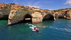 Uma área costeira com uma grande formação rochosa apresentando duas grutas naturais sobre águas azul-claras.