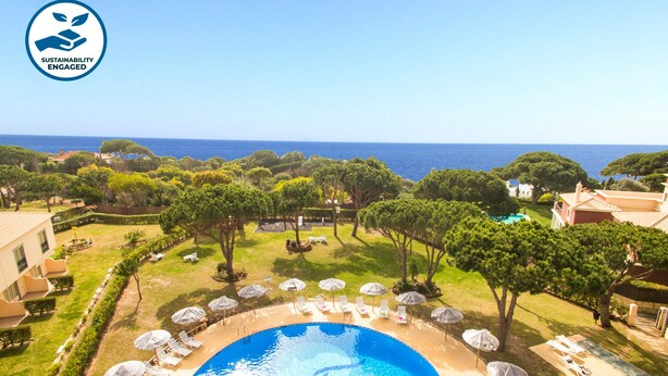 Una piscina rodeada de sillas de descanso y sombrillas, con vistas al mar y árboles.