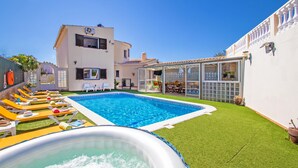 Una piscina con sillones de descanso, un jacuzzi y un edificio con balcón.