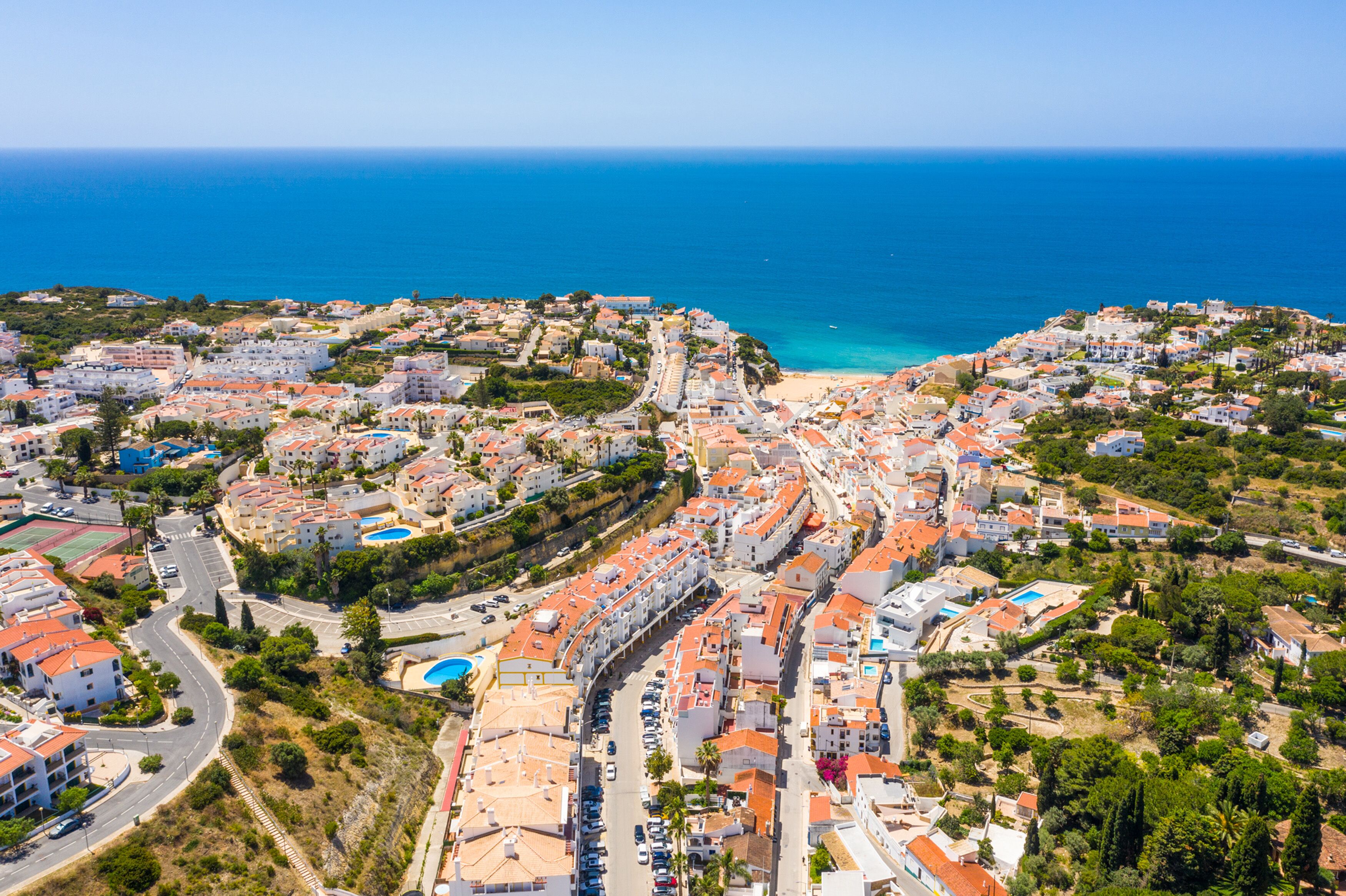 Vista aérea de un pueblo costero con playa, edificios residenciales y un cielo azul despejado.