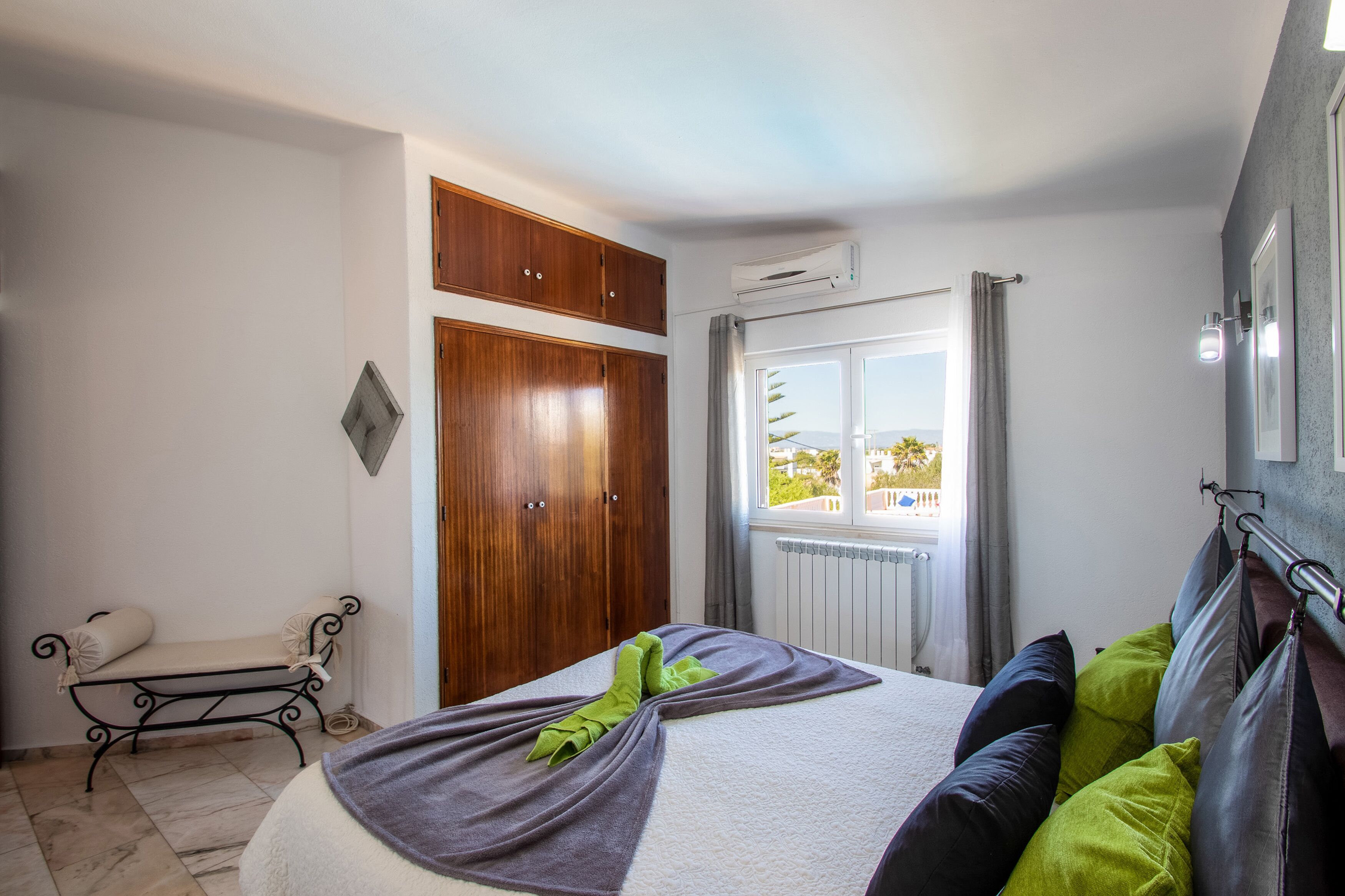 Un dormitorio con cama, un banco, un armario y una ventana con vistas.