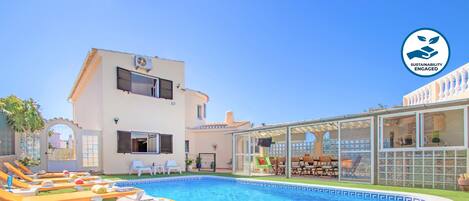A swimming pool with lounge chairs, a covered outdoor seating area, and a building with a balcony.