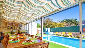 Comedor con vista a la piscina, mesa de madera, sillas y un toldo a rayas.