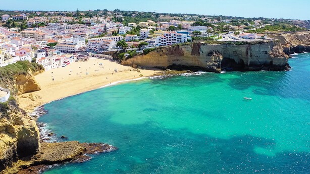 Un pueblo costero con una playa arenosa, aguas turquesas cristalinas y un acantilado rocoso.