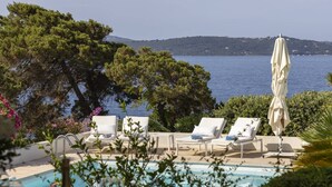 A poolside area with lounge chairs and an umbrella, overlooking a body of water and a distant hill. - VILLA IRIS-Feet in the water, Isolella peninsula, 5 bedrooms, swimming pool, sea view (PIETROSELLA)