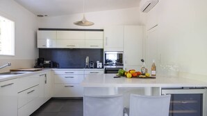 A modern kitchen with white cabinets, a central island, and a dining area with two chairs. - VILLA IRIS-Feet in the water, Isolella peninsula, 5 bedrooms, swimming pool, sea view (PIETROSELLA)