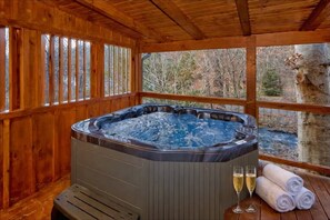 A wooden deck with a hot tub, two glasses of champagne, and rolled towels.