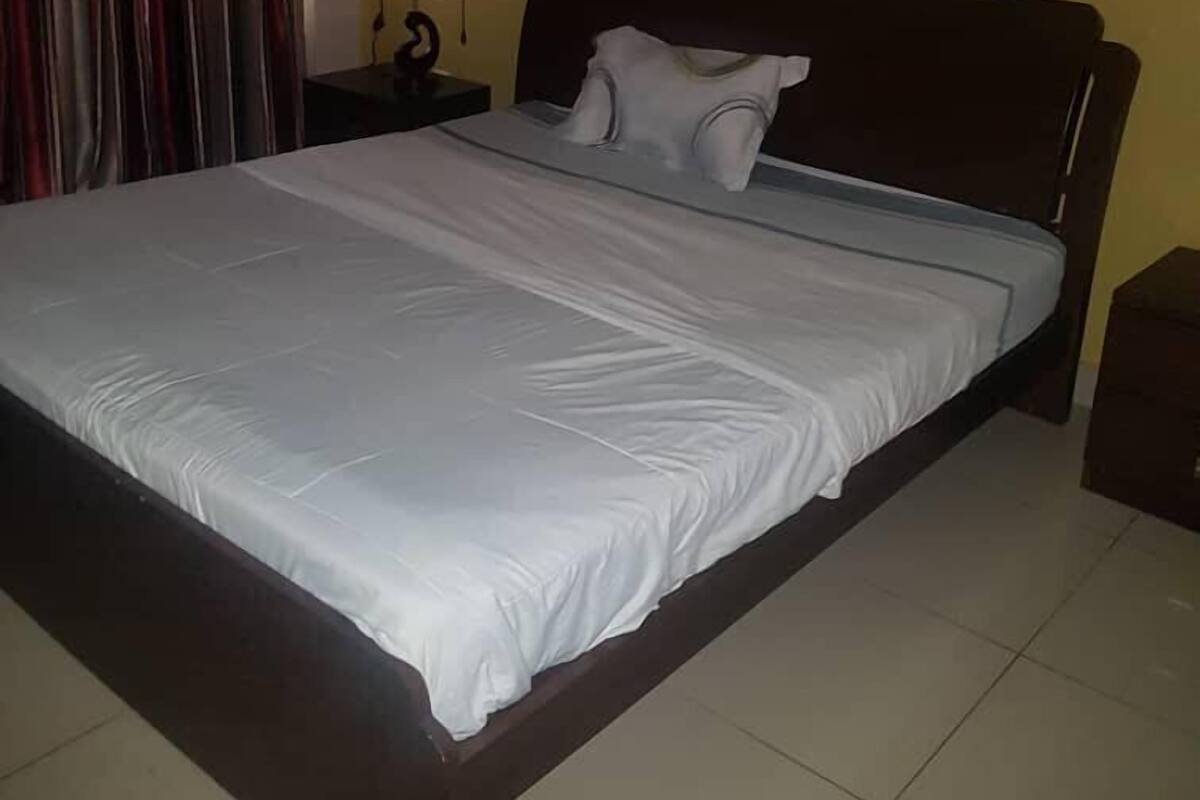 A neatly made bed in a room with yellow walls, a dark wooden headboard, and a curtain on the left.