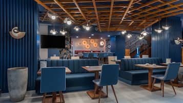 Un interior de restaurante moderno con asientos azules, vigas de techo de madera e iluminación colgante.