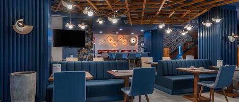 A modern restaurant interior with blue seating, wooden ceiling beams, and pendant lighting.