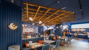 Un restaurante moderno con paredes azules, vigas de madera en el techo y zonas de estar con mesas y sillas.