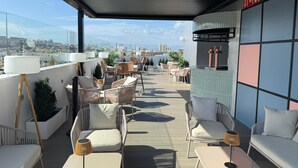 Terraza en la azotea con mobiliario exterior, vistas a la ciudad y un letrero de salida de incendios.