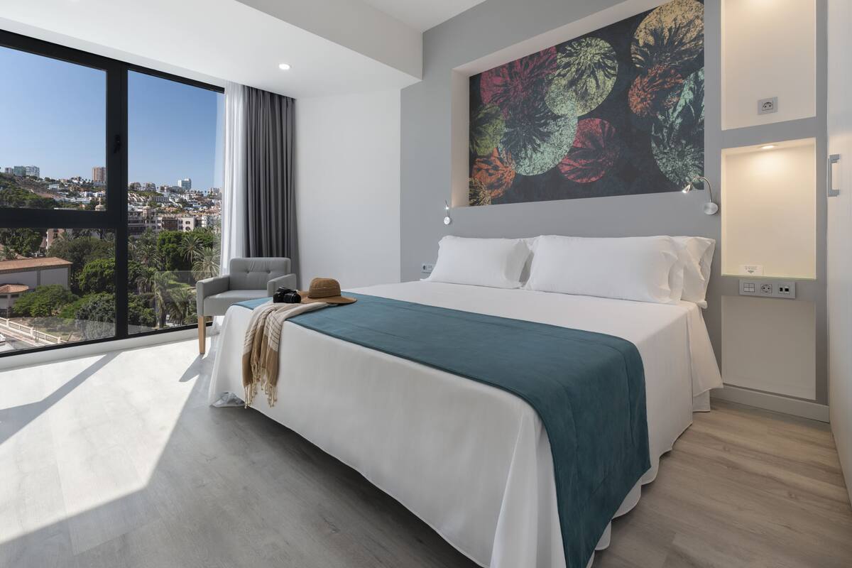 Un dormitorio moderno con una cama grande, vistas de la ciudad y un cuadro de un paisaje urbano en la pared.