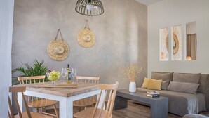 A modern living room with a dining area, featuring a grey textured wall, woven wall art, and a grey sofa with yellow cushions. - Diana Suites (Kefalonia)