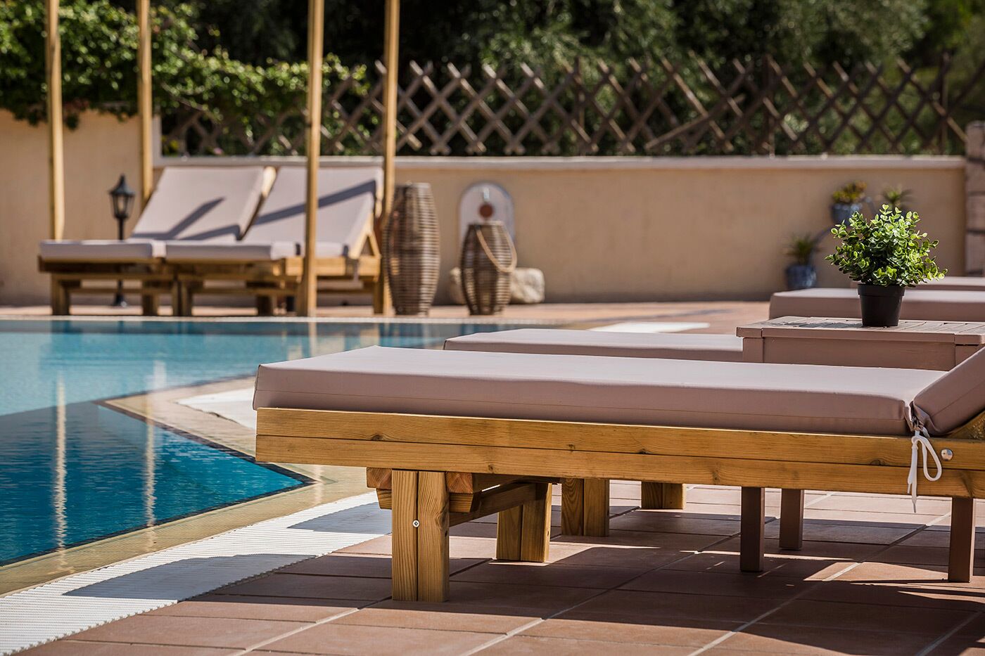 Un espace aménagé au bord de la piscine, avec des chaises longues en bois et une petite plante en pot.