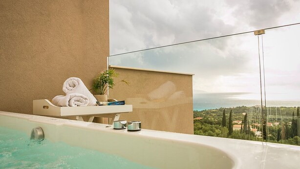 A spa area with a bathtub, towels, a plant, and a view of the sea. - Diana Suites (Kefalonia)