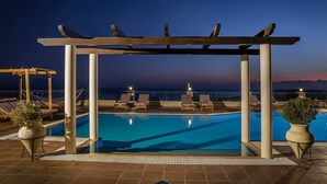 A pool area with lounge chairs and a pergola, overlooking a body of water at dusk. - Diana Suites (Kefalonia)