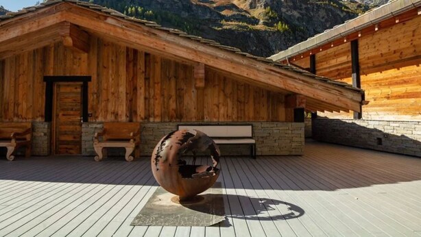A wooden cabin with a sloped roof, stone walls, and a wooden deck. - Chalet Raven Co-living (Tignes)