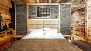 A bedroom with a wooden ceiling, a bed with white linens, a stone wall, and a window with bars. - Chalet Raven Co-living (Tignes)