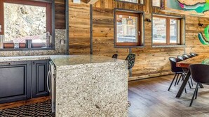 A modern kitchen with granite countertops, wooden cabinetry, and a dining area with a wooden table and chairs. - Chalet Raven Co-living (Tignes)