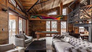 A cozy cabin interior with a pool table, plush seating, and large windows offering views of the surrounding forest. - Chalet Raven Co-living (Tignes)