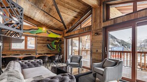 A cozy room with a large bed, a sofa, and two armchairs. There is a wooden ceiling with exposed beams and a large window offering a view of the outdoors. - Chalet Raven Co-living (Tignes)