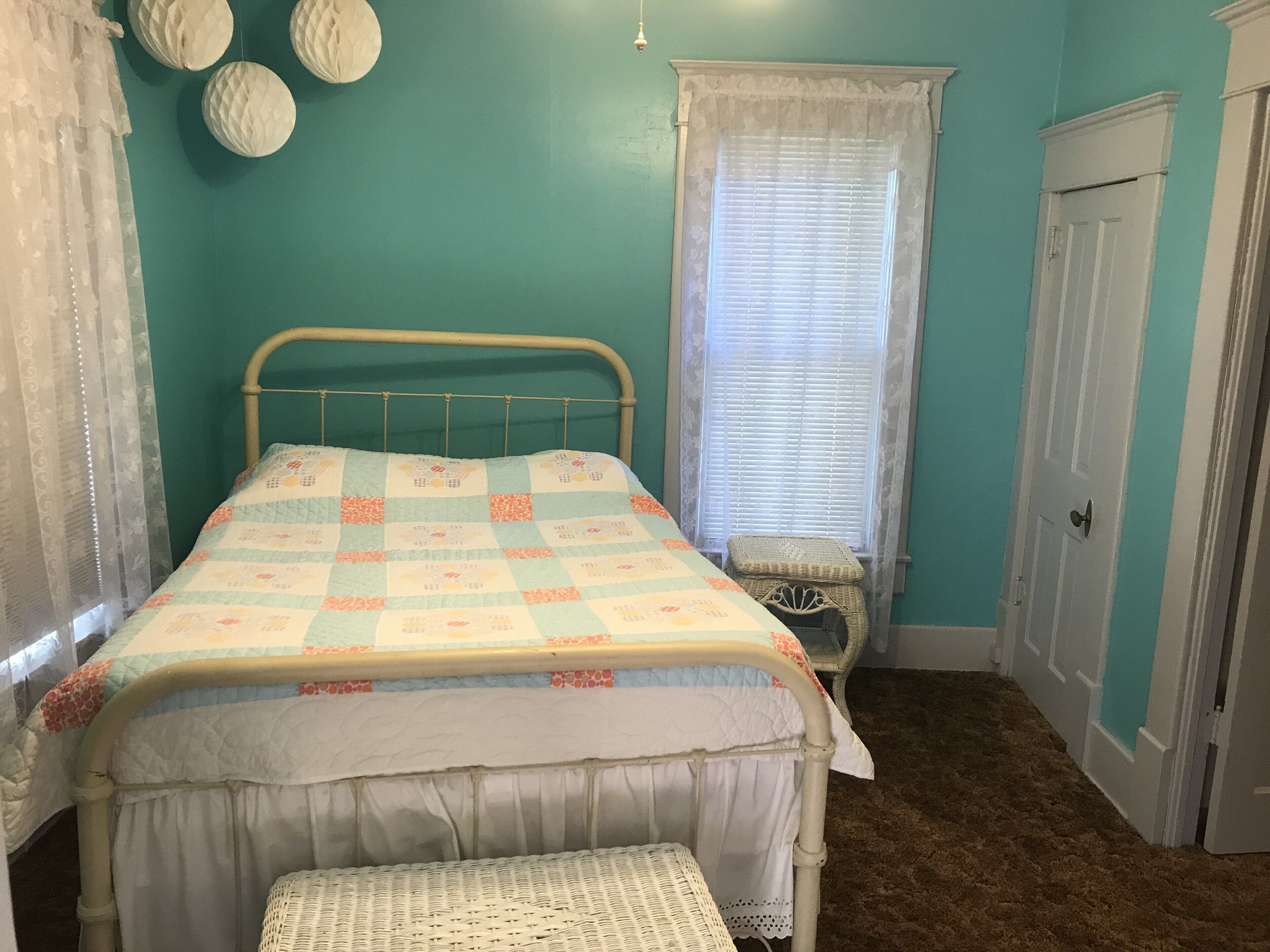 Une chambre à coucher avec un lit, une fenêtre avec des stores, une porte et un petit banc.