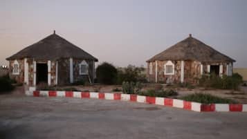 Two small, single-story buildings with thatched roofs and stone walls, surrounded by a red and white painted curb.