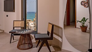 Un balcón con una mesa de ajedrez, dos sillas, un televisor y vista al mar.