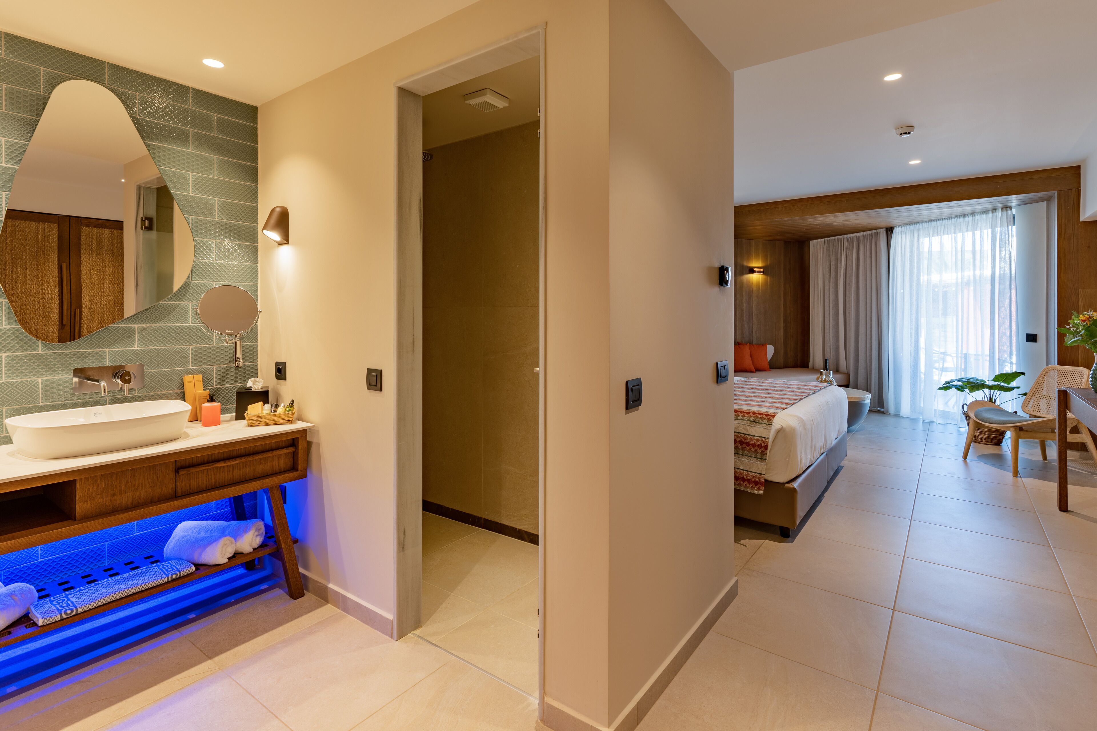 A modern hotel room with a bathroom, a bed, and a seating area.