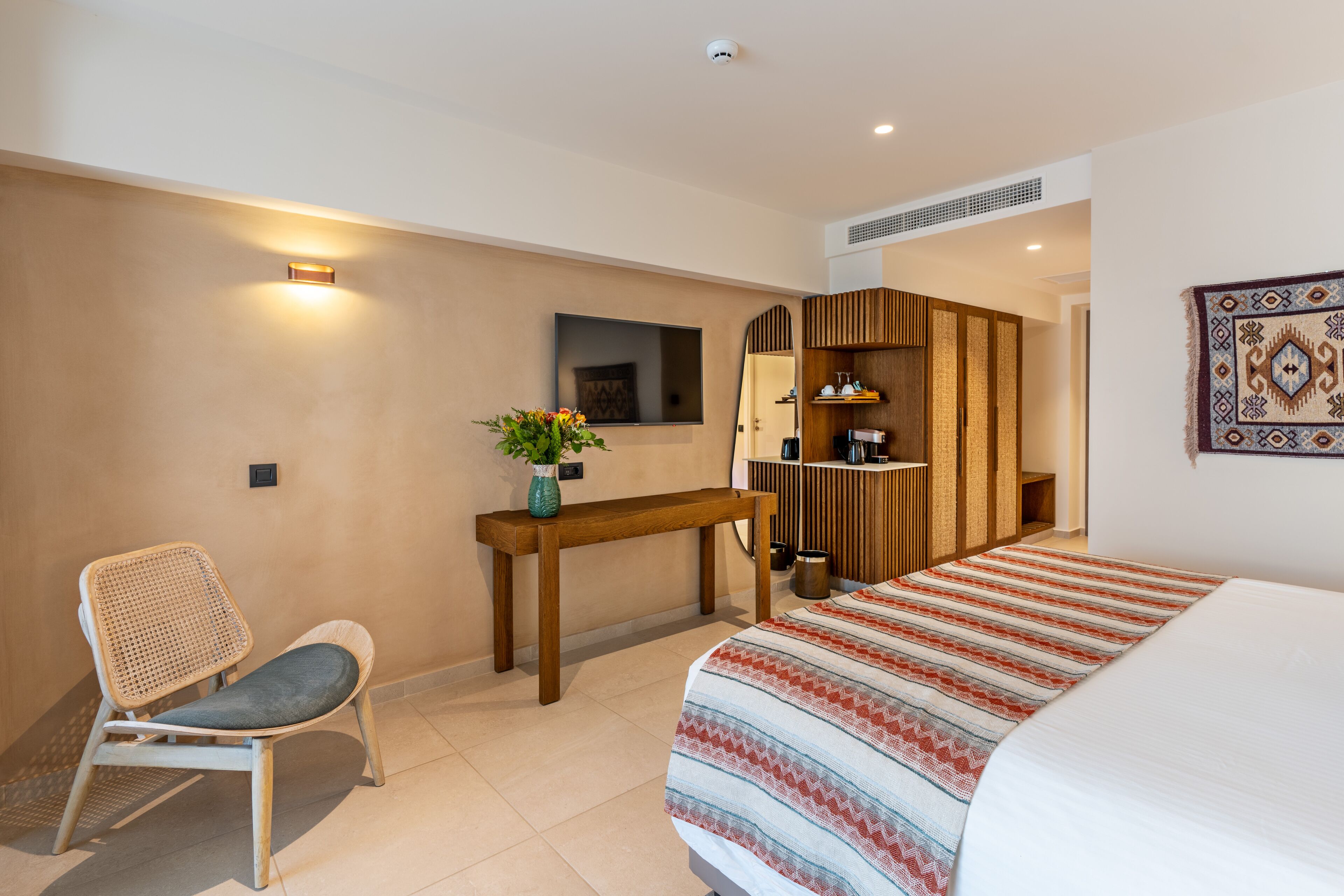 A hotel room with a bed, a desk, a chair, a mirror, and a wall-mounted TV.