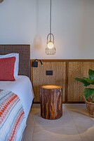 Una camera d'albergo con un letto, uno sgabello di legno, una lampada a sospensione e una pianta.