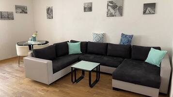 Un salon moderne avec un canapé d’angle, une petite table basse et une table ronde avec des chaises.