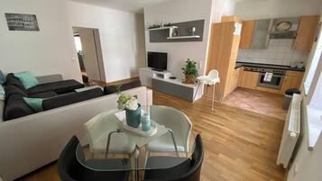 Uma sala de estar moderna com sofá, mesa de jantar com cadeiras, TV e área de cozinha com armários e fogão.