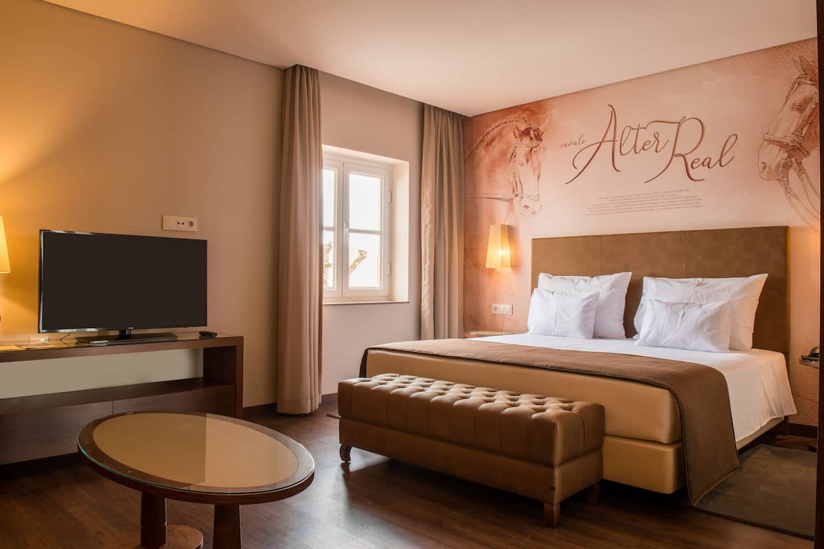 A hotel room with a bed, a television on a stand, a round glass table, and a wall with a horse illustration and text.