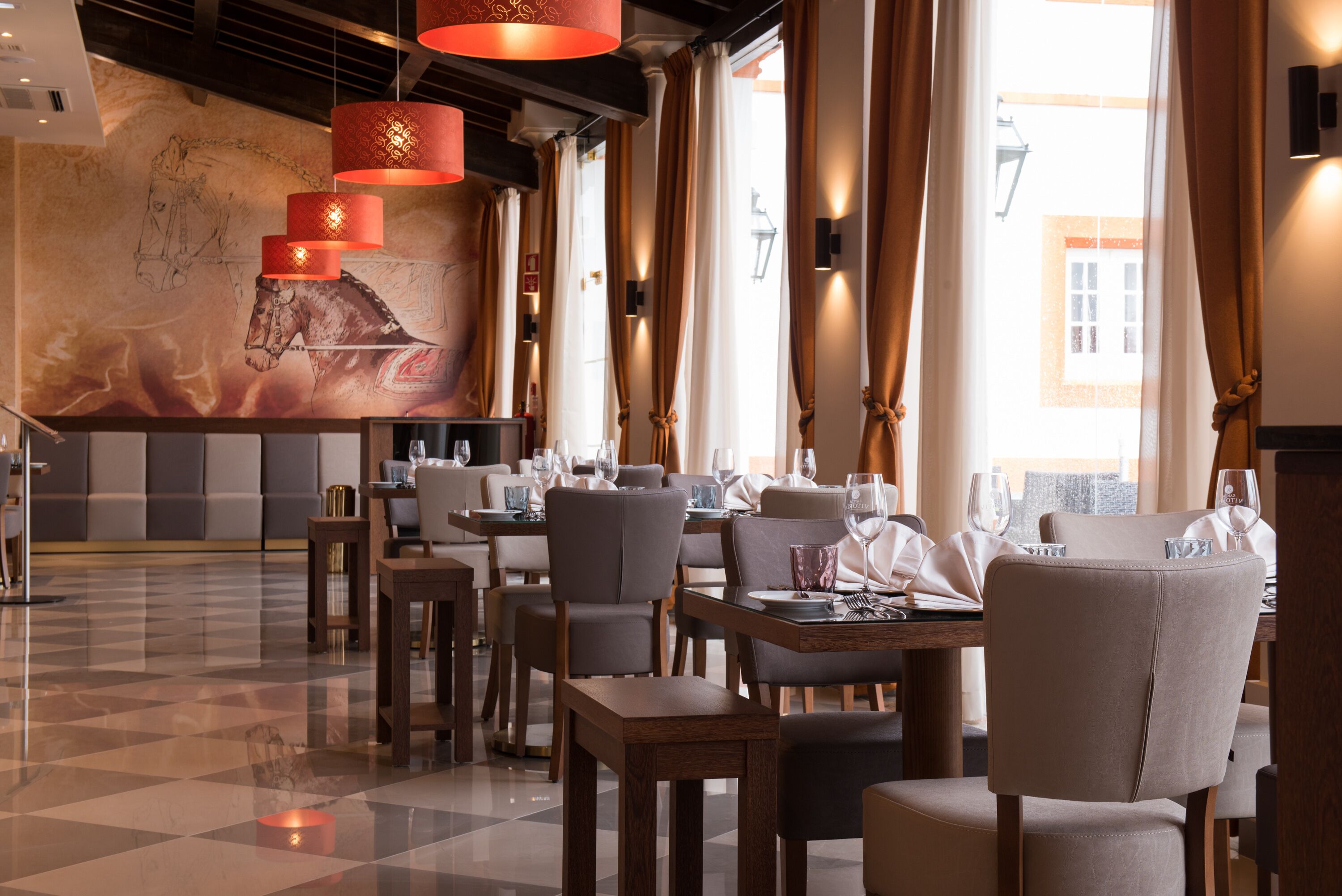 A restaurant with a checkered floor, dining tables, chairs, and hanging red lamps.