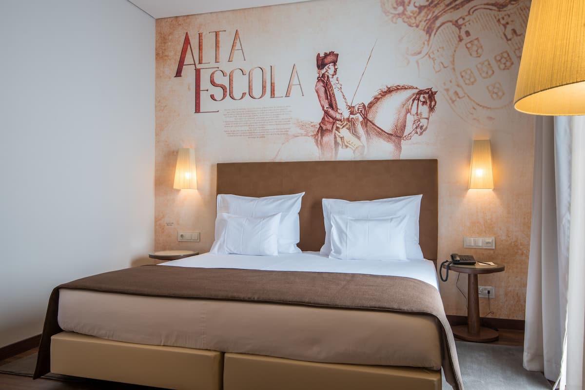 A hotel room with a large bed, two bedside lamps, a wall-mounted artwork, and a small table with a phone.