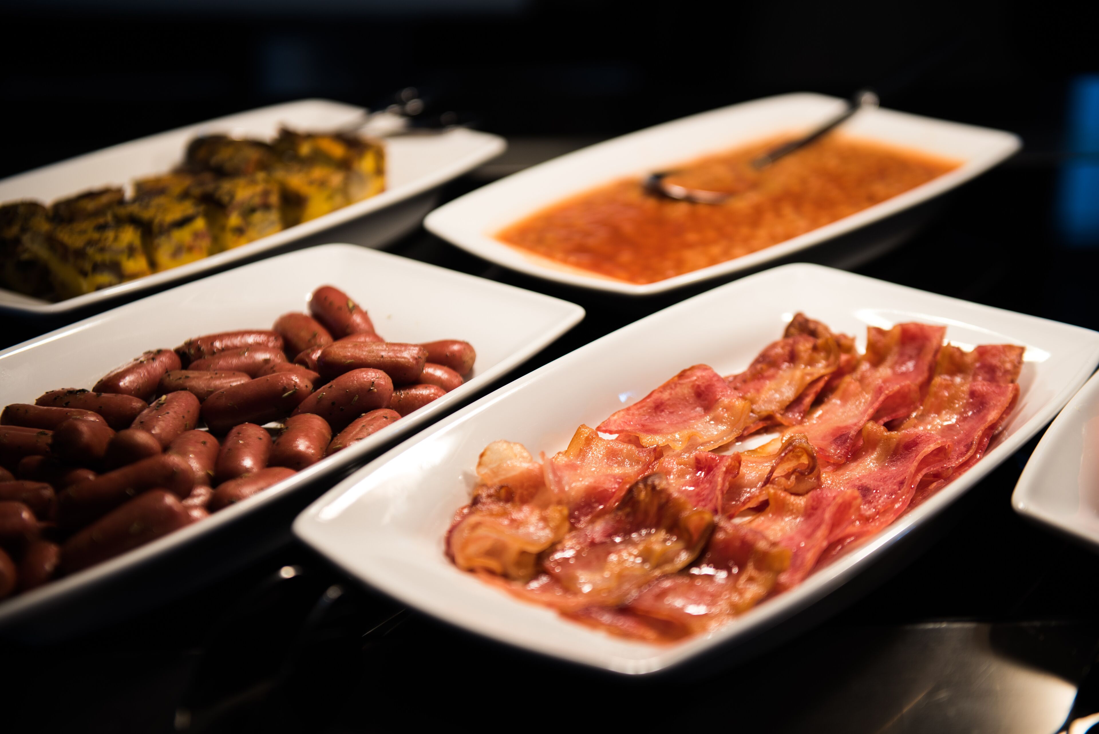 A buffet with various dishes including sausages, a meat dish, and a vegetable dish.
