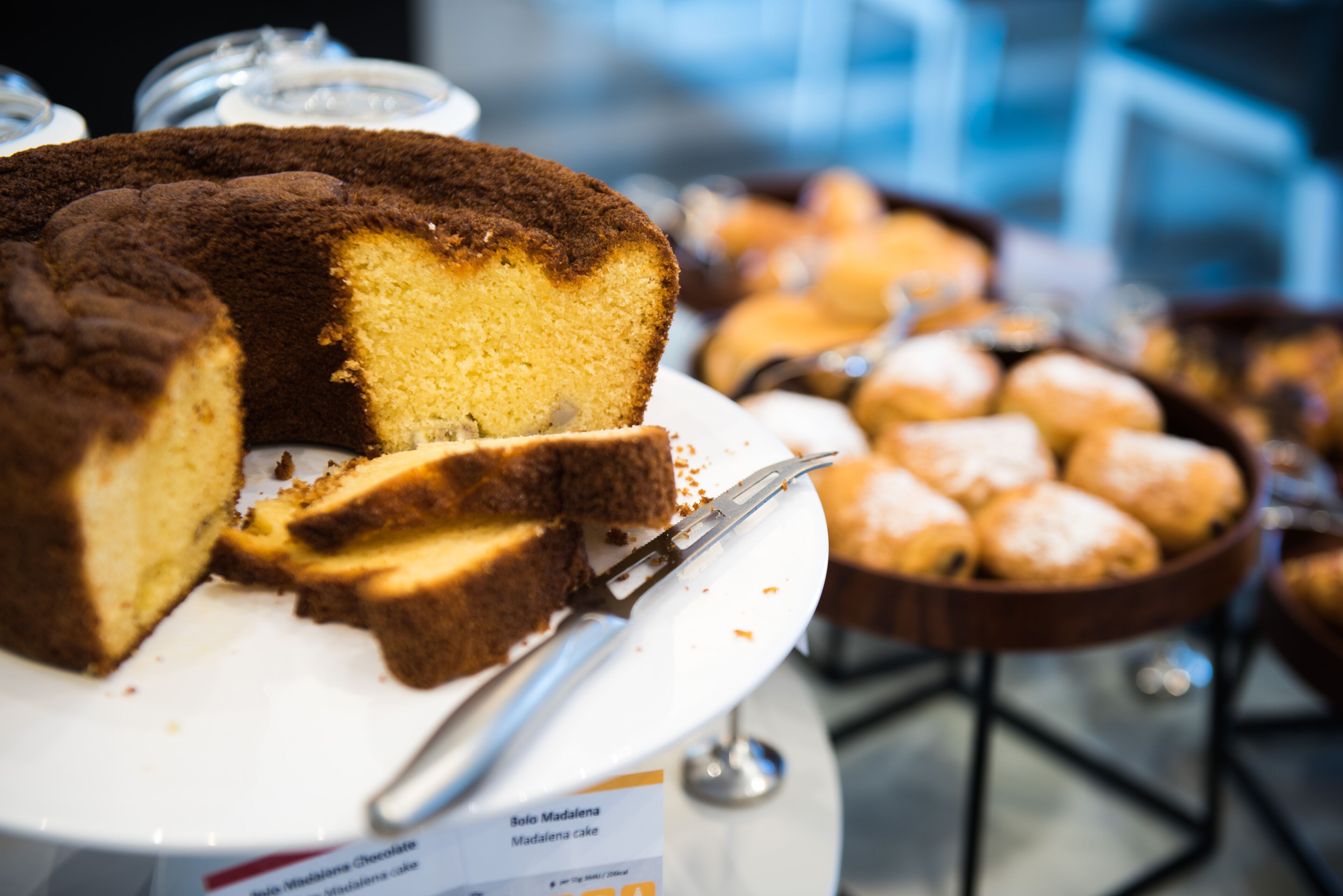 A cake with a slice cut out, a knife on the plate, and a sign indicating it is a Madalenka cake.