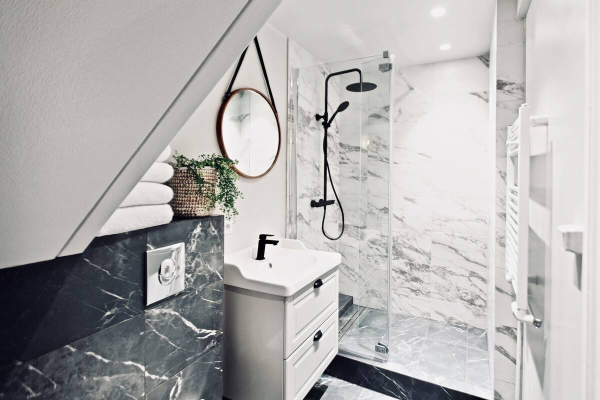 A modern bathroom with a marble sink, a glass shower enclosure, and a white vanity.