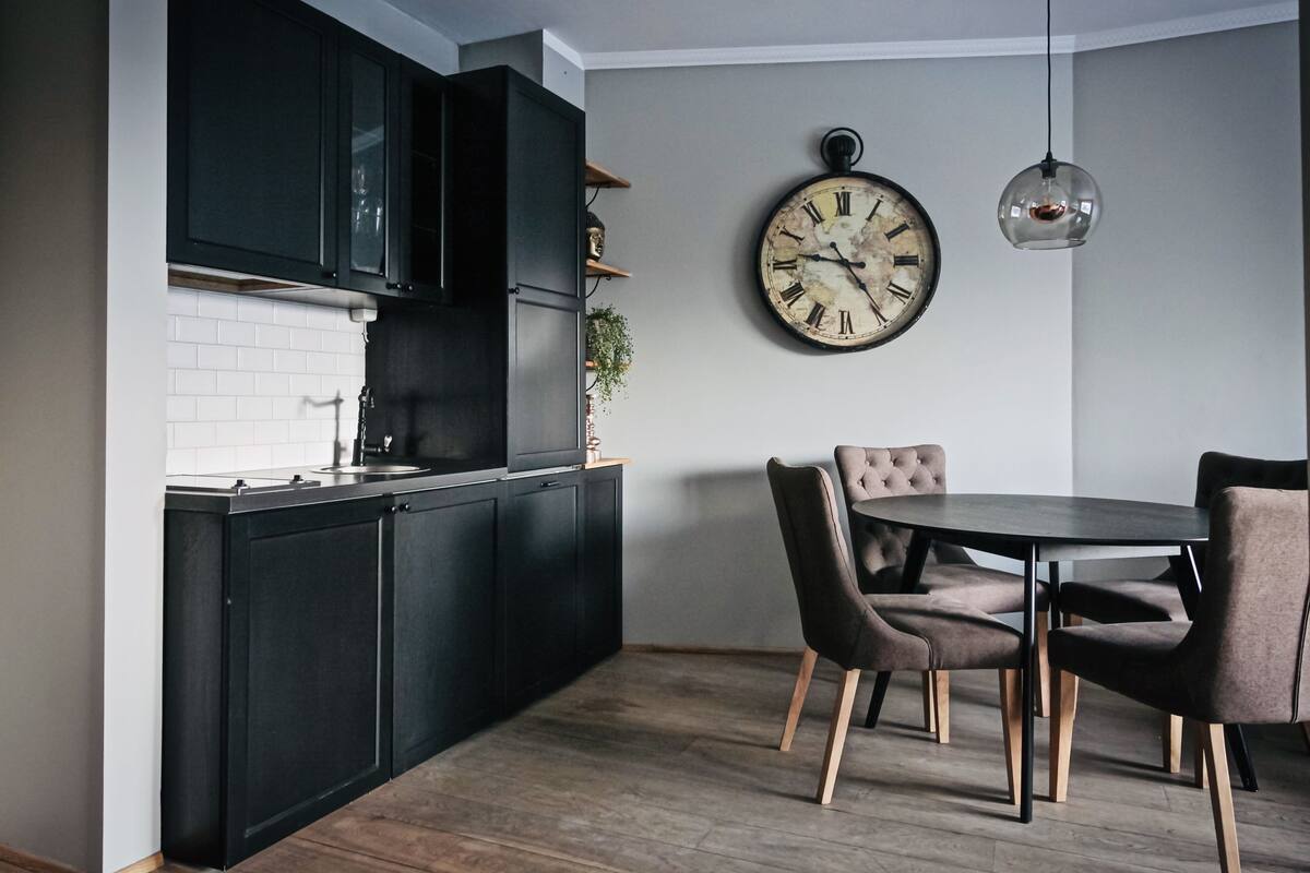 A modern kitchen with dark cabinets, a white tiled backsplash, and a dining area with a round table and four chairs.
