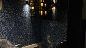 A bathroom with blue mosaic tiles, a bathtub, and a shelf with candles. - Heart of Reykjavik (Reykjavik)