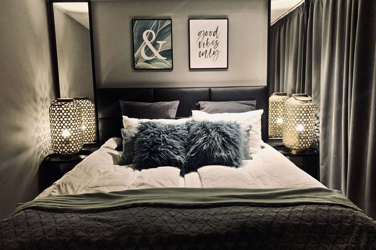 A neatly made bed with a fluffy pillow, two framed artworks on the wall, and two lamps on either side.