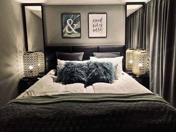 A neatly made bed with a fluffy pillow, two framed artworks on the wall, and two lamps on either side.
